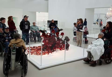 Veterans viewing a deep red glass art sculpture.